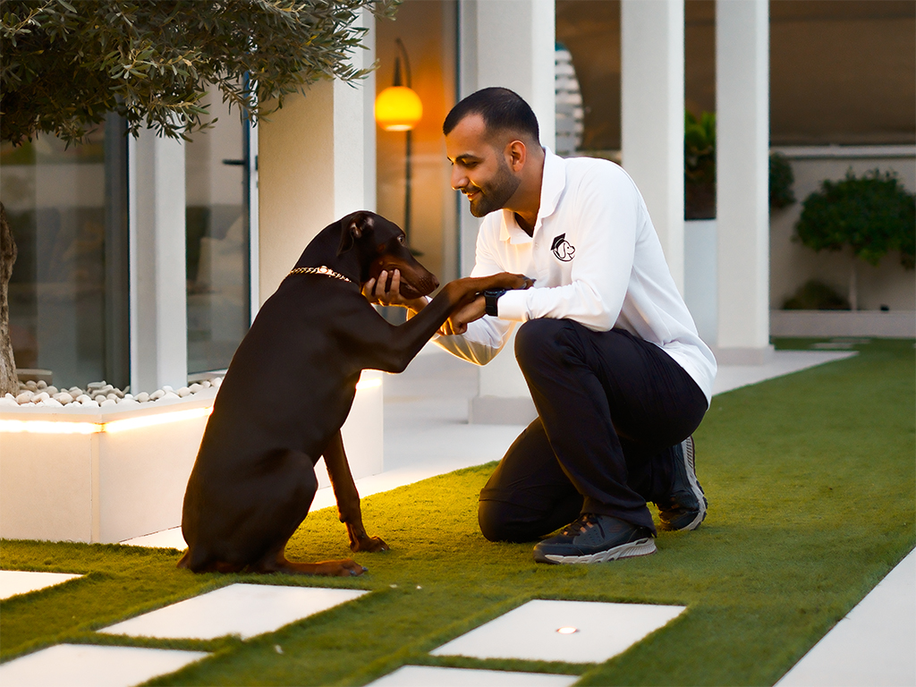 Professional dog trainer sharing a friendly moment with a Doberman outdoors in Dubai