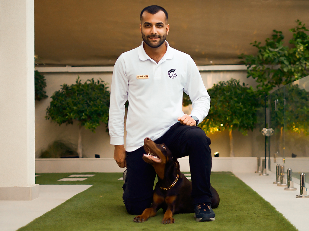 Professional dog trainer kneeling beside a Doberman during an outdoor training session in Dubai